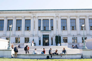 Several people sitting around the steps of Doe Library