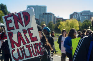 A person at a protest holds a sign that says "end rape culture"